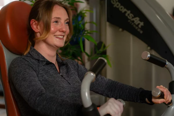 Eine lächelnde Frau trainiert an einem Fitnessgerät im Physioaktiv Sportsclub und blickt motiviert zur Seite.